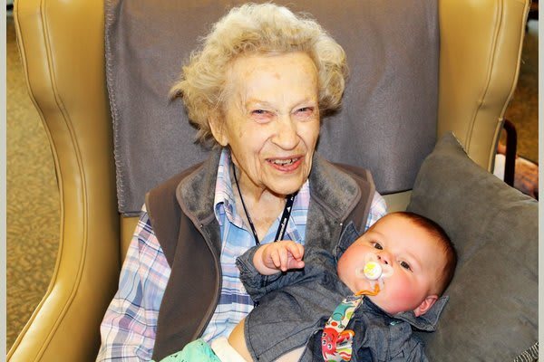 An elderly woman smiling while holding a baby, showcasing a moment of family bonding.