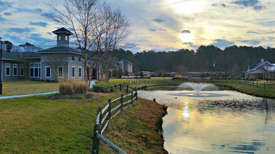 A serene view of a building beside a pond with a fountain, reflecting the colorful sunset sky.