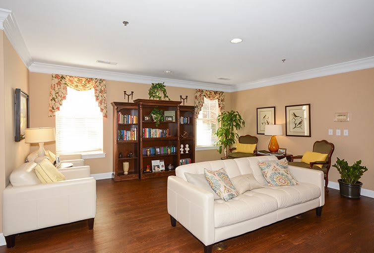 A cozy living room with a cream sofa, bookshelf, and wooden flooring, warmly lit by natural light.