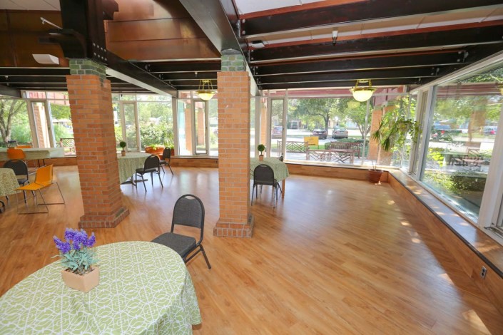 A bright indoor event space with tables and chairs, featuring large windows and a wooden floor.