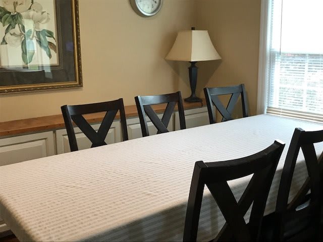 A dining room with a table, chairs, and a lamp under a wall clock.