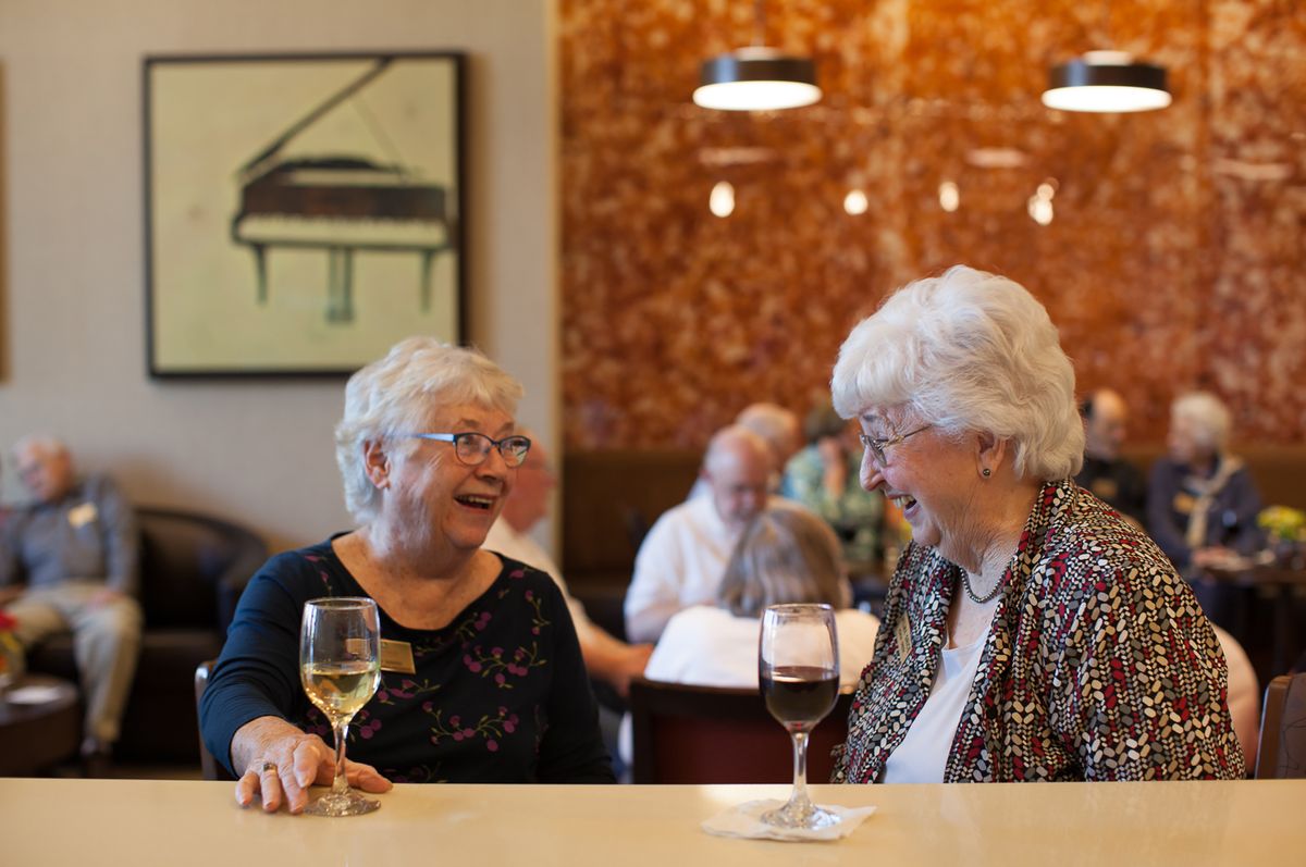 Two elderly women enjoy a lively conversation over wine in a cozy restaurant setting.