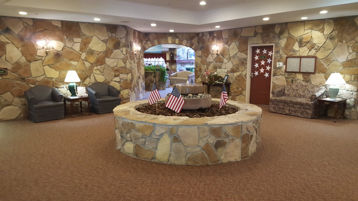 A cozy indoor lobby featuring a stone fountain adorned with small flags, surrounded by stone walls and seating.