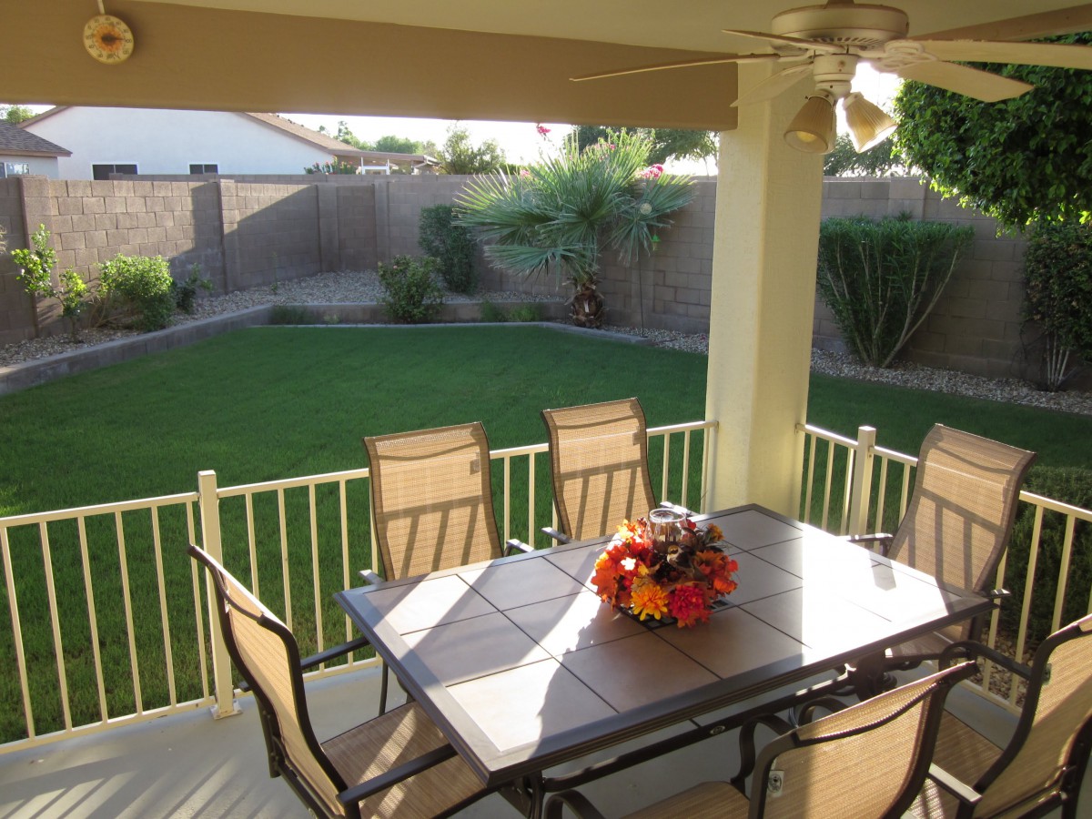 A cozy backyard patio with a table and chairs, overlooking a well-maintained lawn and garden.