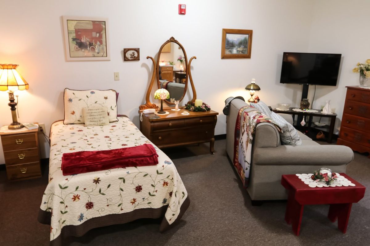 A cozy bedroom featuring a single bed with floral bedding, a vintage dresser with a mirror, and a comfortable sofa.