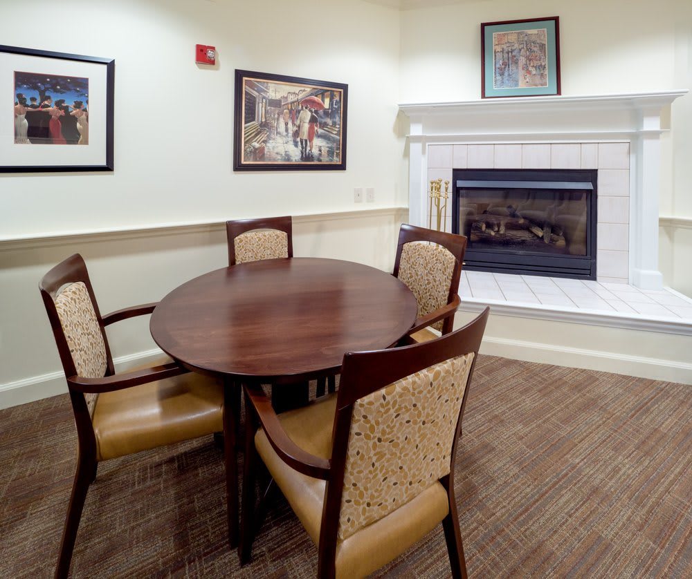 A cozy dining area featuring a round table with four chairs, a fireplace, and framed artwork on the walls.