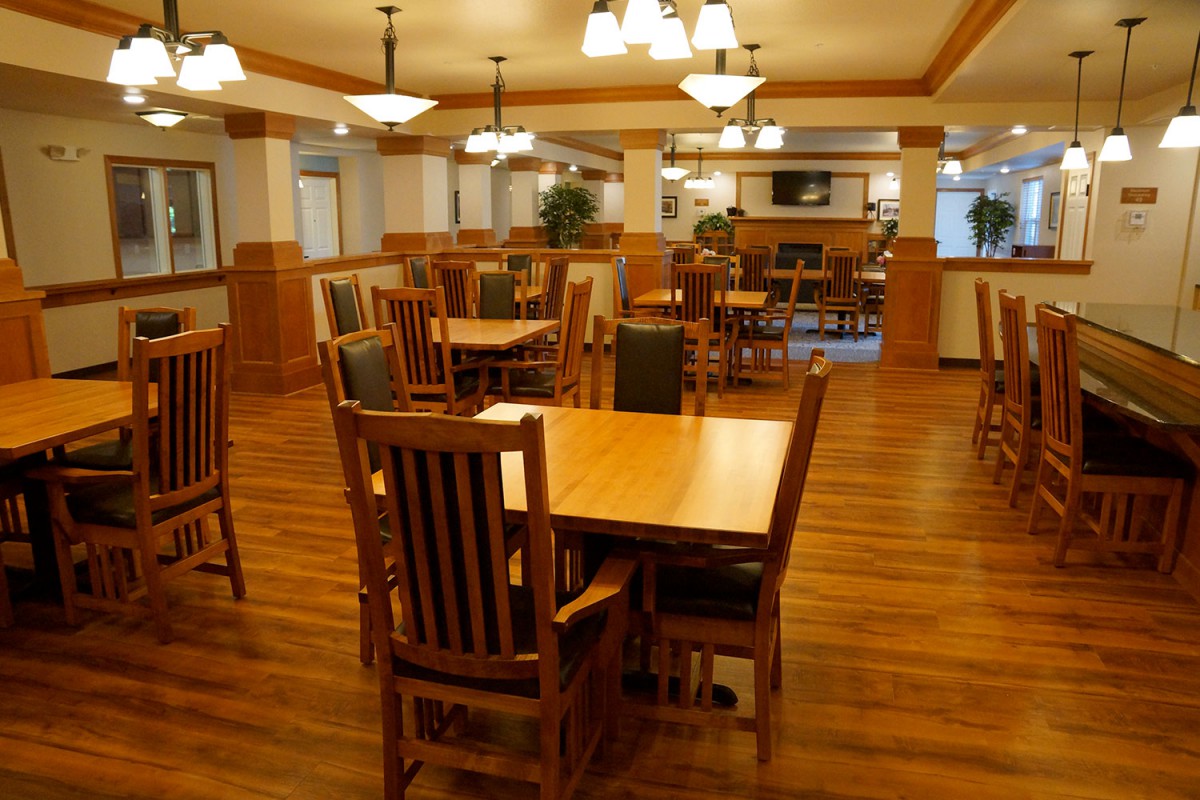 An empty restaurant dining area with wooden tables and chairs, well-lit by overhead lighting fixtures.
