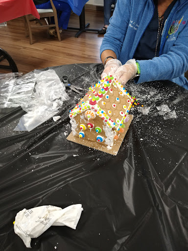 A festive gingerbread house is being decorated with colorful candies during a holiday crafting session.