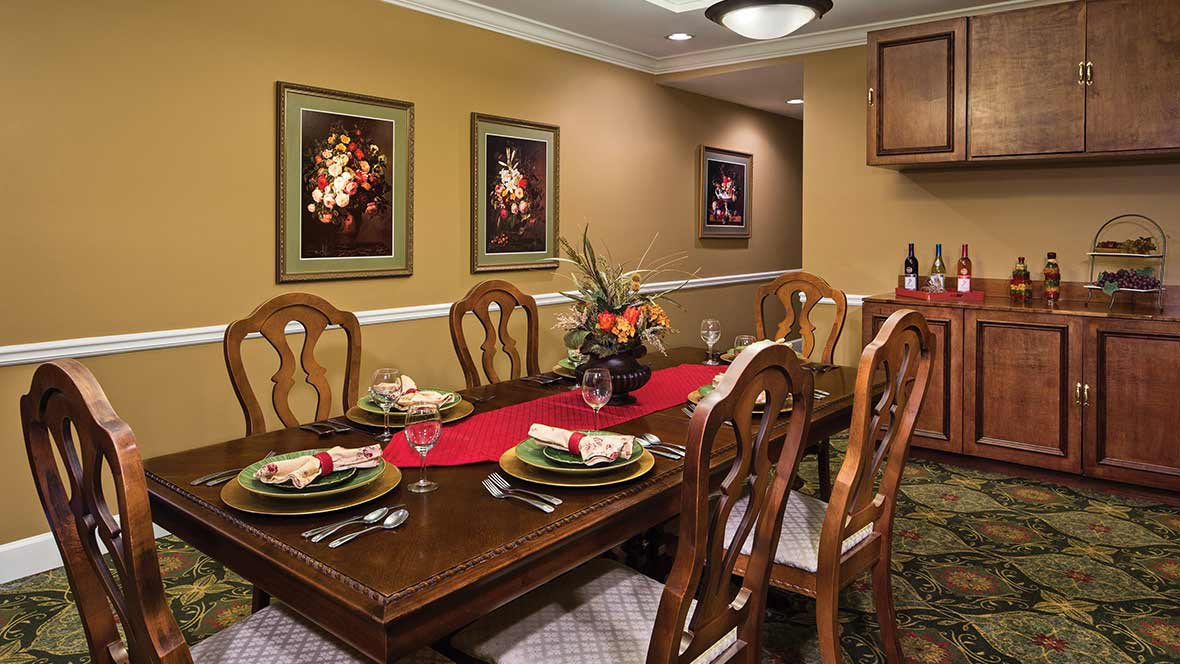 A well-decorated dining room with a wooden table set for a meal, surrounded by chairs and adorned with floral centerpiece and artwork on the walls.