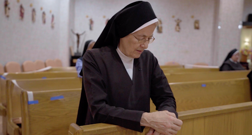 A nun in prayer, reflecting in a tranquil church setting.