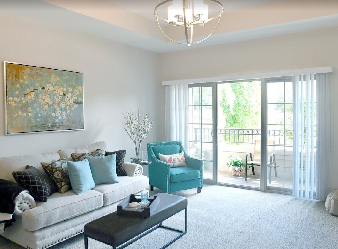A modern living room with a comfortable sofa, teal armchair, and large windows leading to a balcony.