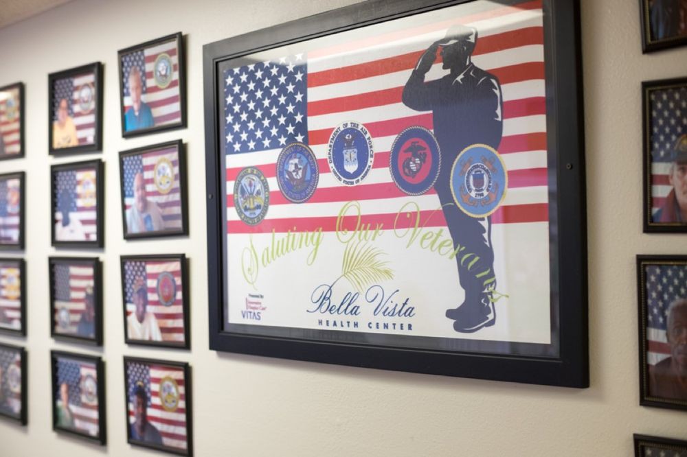 Framed military-themed artwork featuring the American flag and various service emblems on a wall.