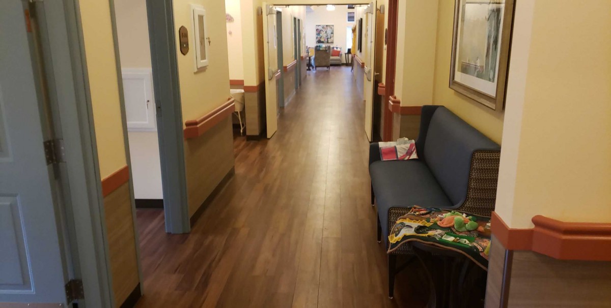 A long hallway with wooden flooring and seating along the side, resembling a healthcare facility.