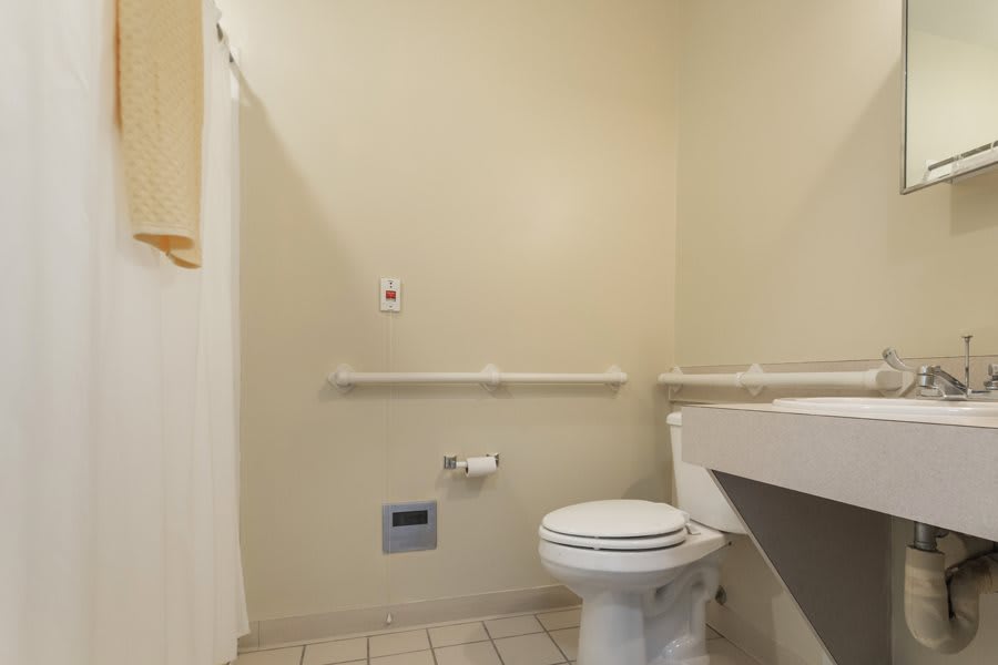 An accessible bathroom featuring a toilet, sink, handrails, and tile flooring.