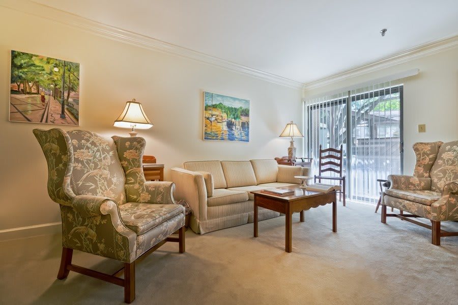 A cozy living room featuring a comfortable sofa, armchair, and coffee table, illuminated by lamps with sliding glass doors in the background.