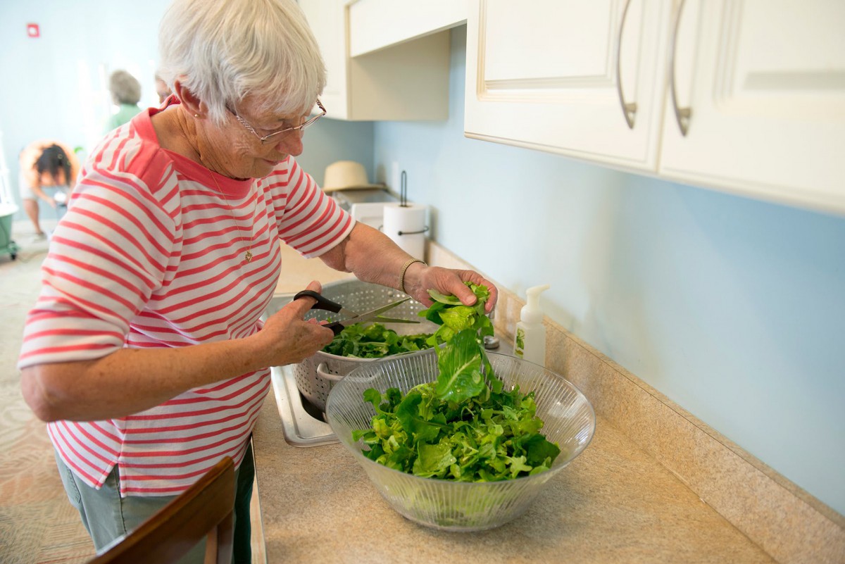 An elderly woman preparing a fresh salad in the kitchen.