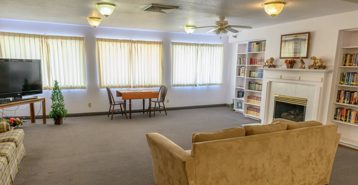 A cozy living room featuring a sofa, table with chairs, and a bookshelf by the windows.