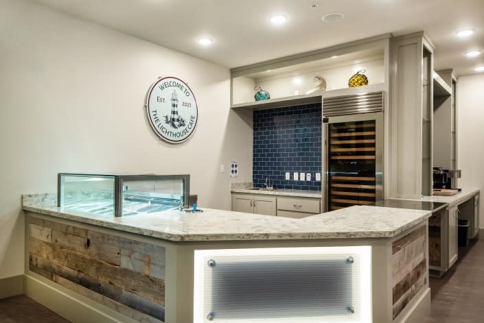 A modern reception area featuring a counter with a display case, a large clock on the wall, and a beverage cooler.