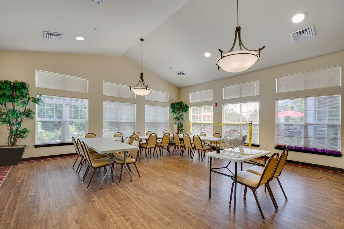 A spacious dining room with multiple tables and chairs, featuring large windows and elegant chandeliers.