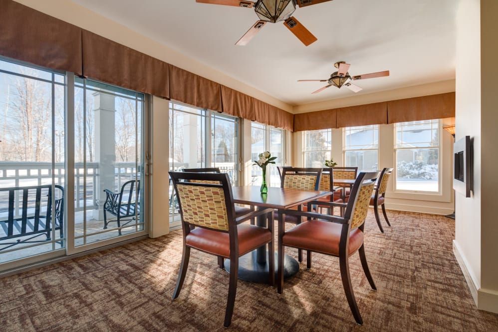 A well-lit dining area with a table and chairs, surrounded by large windows and equipped with ceiling fans.