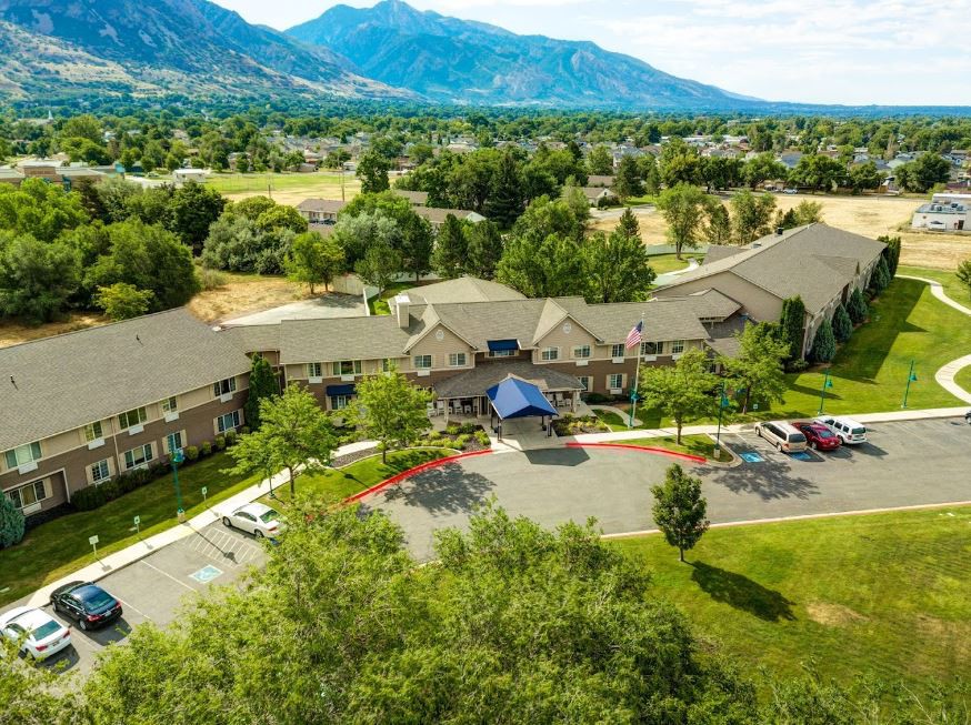 An aerial view of a building surrounded by greenery with mountains in the background.