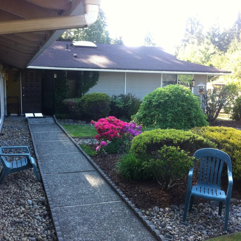 A serene garden path leading to a house, surrounded by colorful flowers and shrubs.