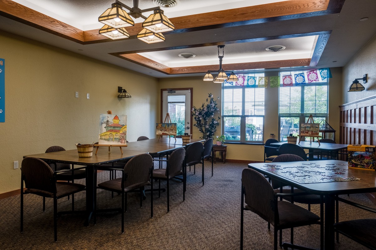 A cozy dining room with large windows, neatly arranged tables and chairs, and decorative lighting.