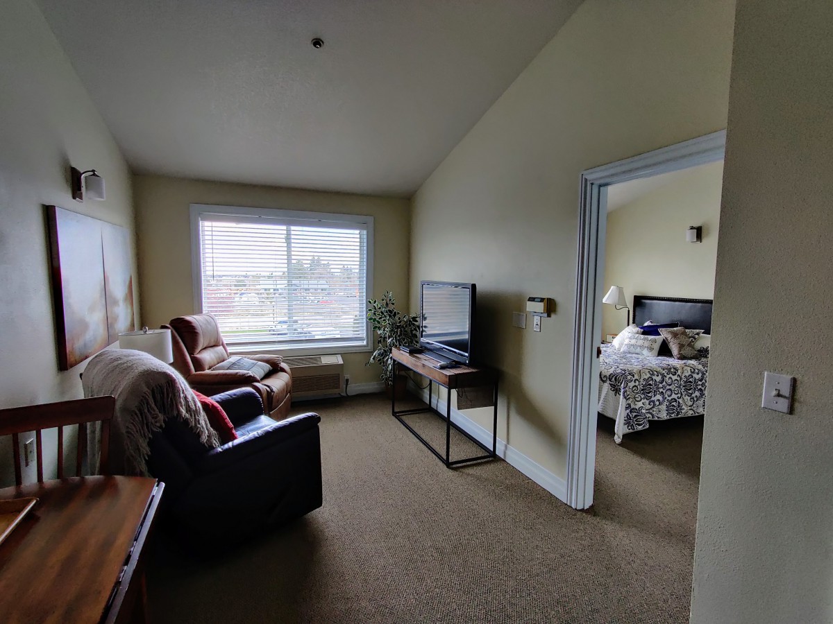 A cozy living area with an adjoining bedroom, featuring a television, armchair, and window view.
