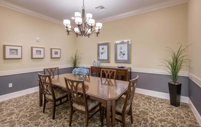 A classic dining room with a large wooden table, surrounded by chairs, under a decorative chandelier.