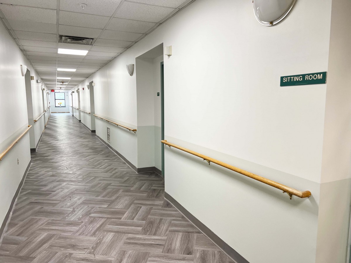 An empty hospital corridor with white walls and handrails.