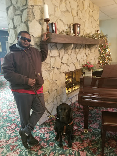 A man poses confidently beside a black labrador dog in a cozy indoor setting decorated for the holidays.