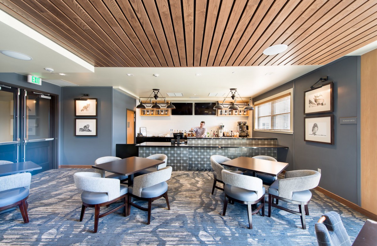 A modern cafe interior featuring a wooden ceiling, elegant seating, and a stylish bar area.