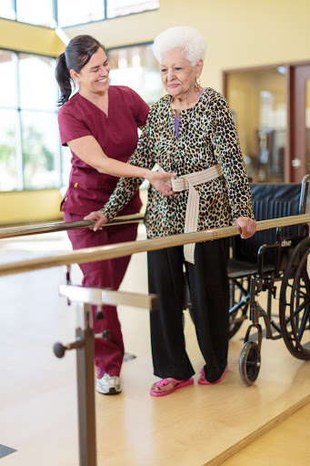 A nurse assists an elderly patient in a rehabilitation setting, supporting her as she practices walking using a rail.