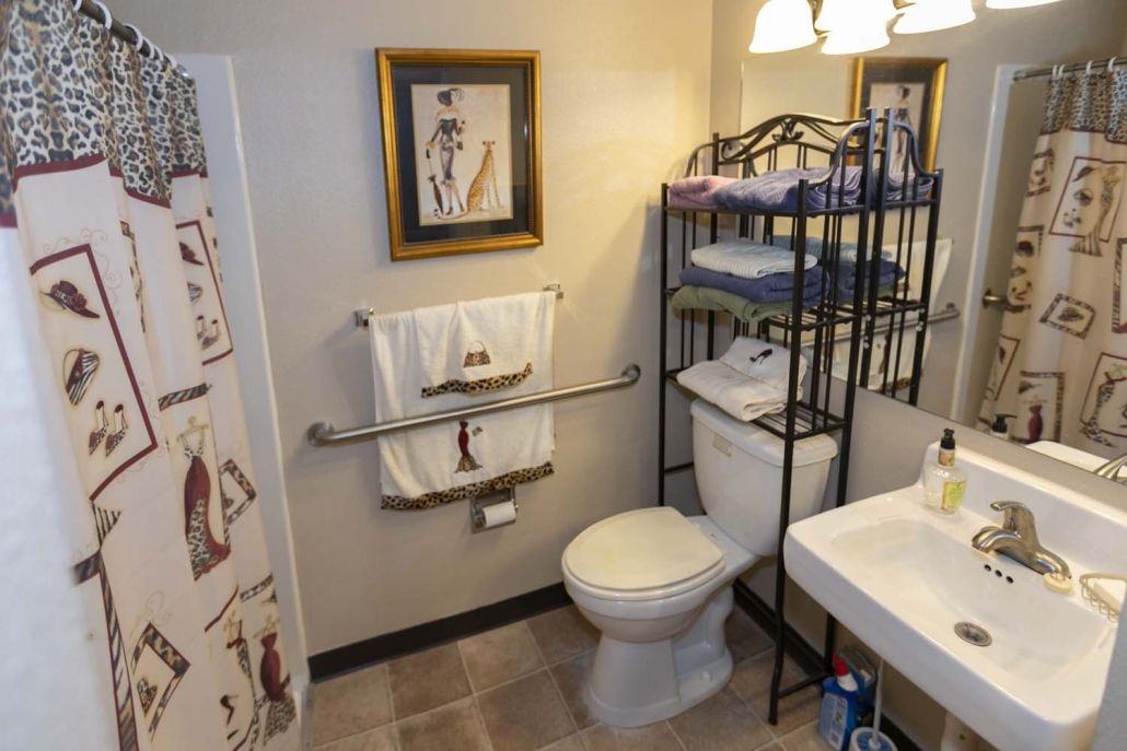 A neatly organized bathroom featuring a toilet, sink, shelving with towels, and decorative elements.