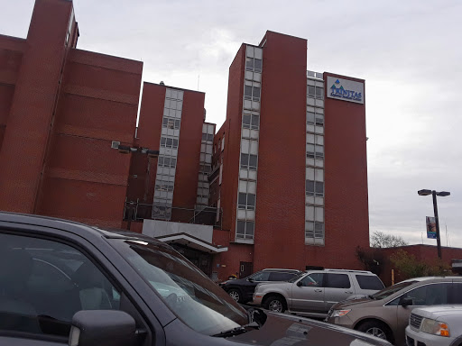 A view of a brick apartment building with multiple floors, parked cars in the foreground.