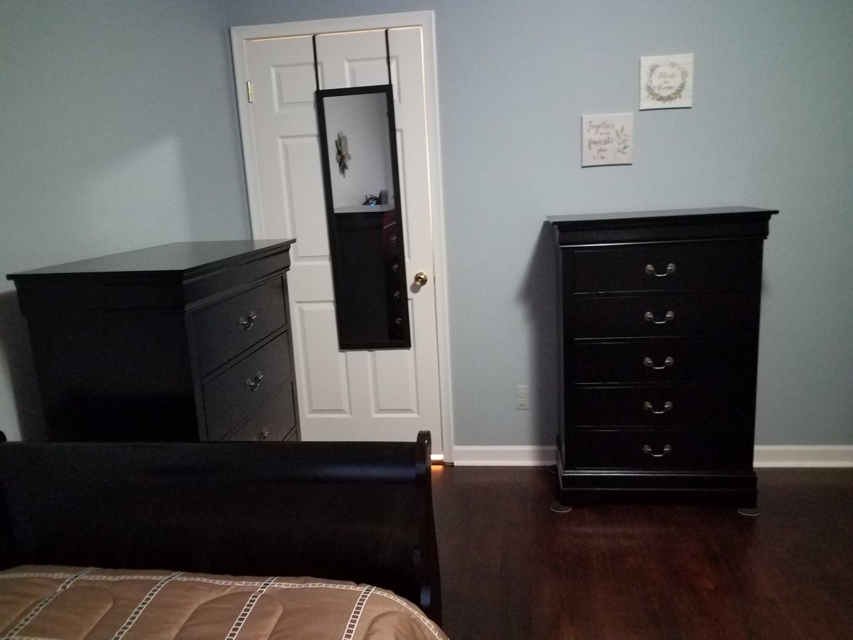 A neatly organized bedroom with dark wood furniture and a door-mounted mirror.