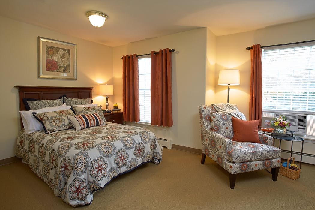 A cozy bedroom featuring a patterned bedspread, matching armchair, and warm lighting.