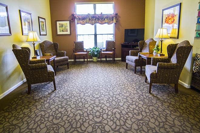 A cozy living room with several chairs and tables, a patterned carpet, and a window letting in natural light.
