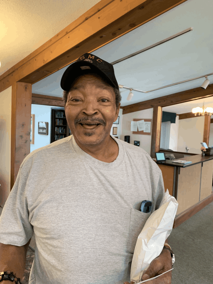 A smiling man wearing a hat and casual clothing indoors.