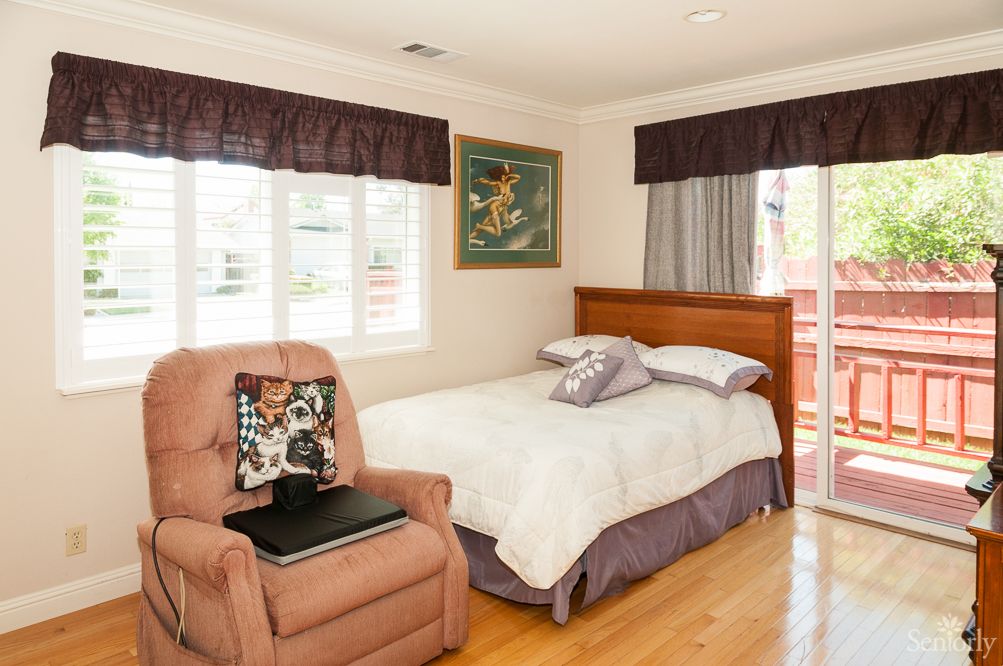 A cozy bedroom with a single bed, an armchair, and window curtains.