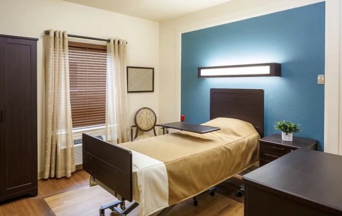 A modern hospital room with a single bed, blue accent wall, and wooden flooring.
