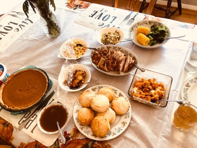 A delicious home-cooked meal spread on a table, featuring an assortment of dishes including bread rolls, gravy, vegetables, and meat.