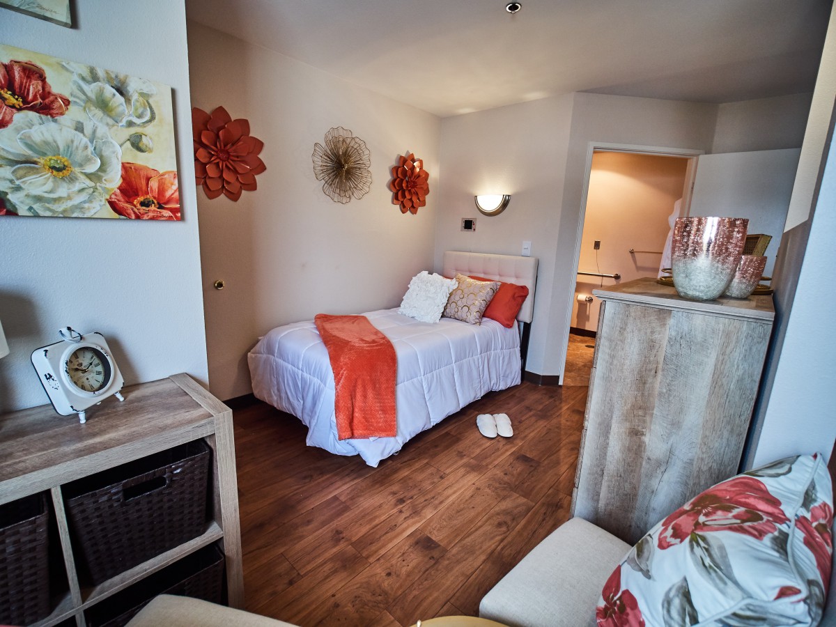 A cozy bedroom featuring a single bed with orange accents and wood flooring.