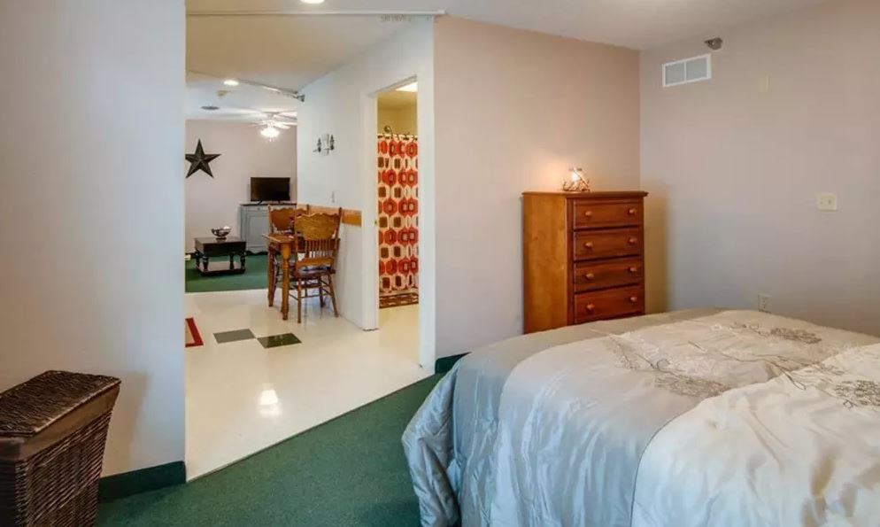 A cozy apartment interior featuring a bedroom with a dresser and a glimpse into a living room area.