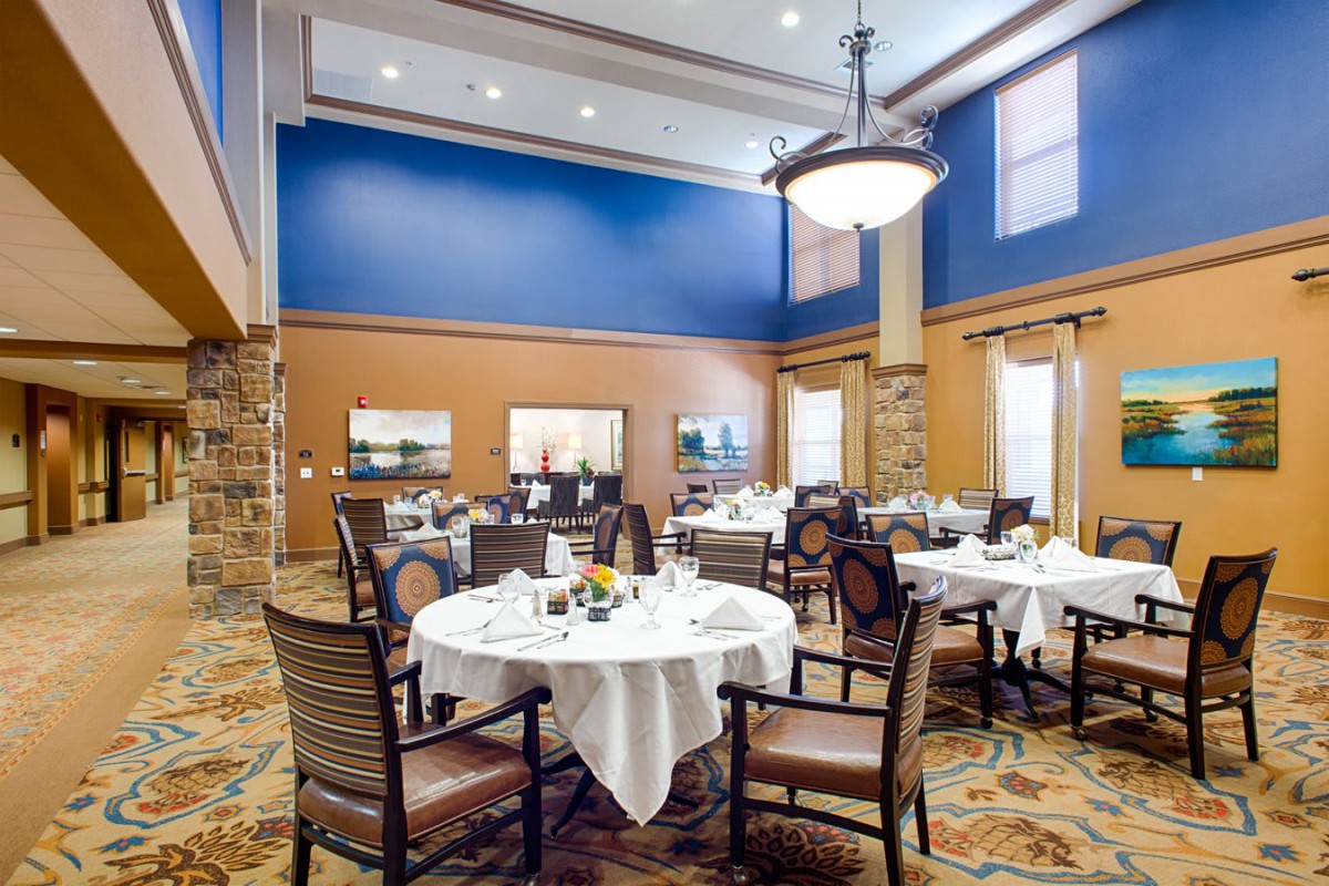 A beautifully designed dining room with elegantly set tables and comfortable chairs under a grand chandelier.