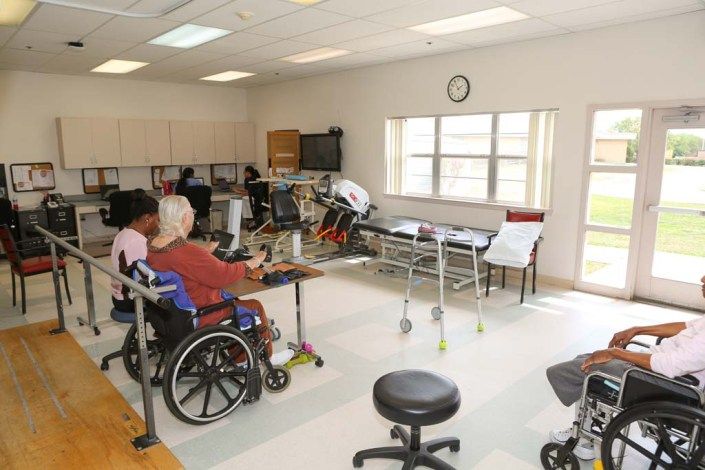 A rehabilitation room equipped for physical therapy with elderly individuals in wheelchairs.