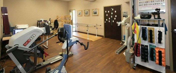 A rehabilitation room equipped with exercise machines and parallel bars.