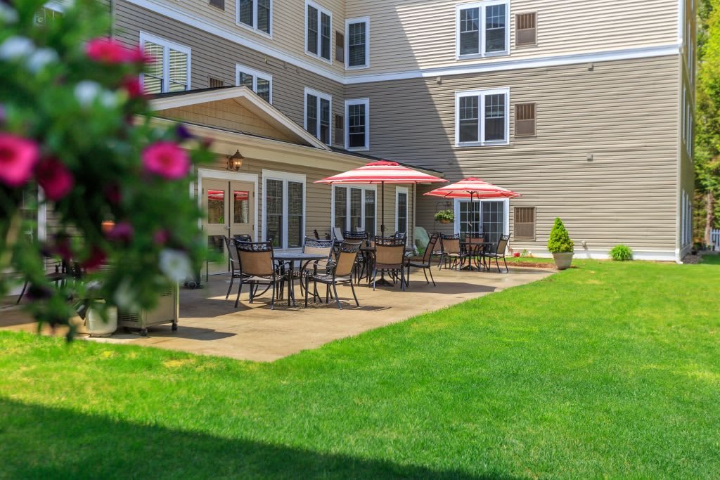 A building with a patio featuring tables, chairs, and sun umbrellas next to a well-maintained lawn.
