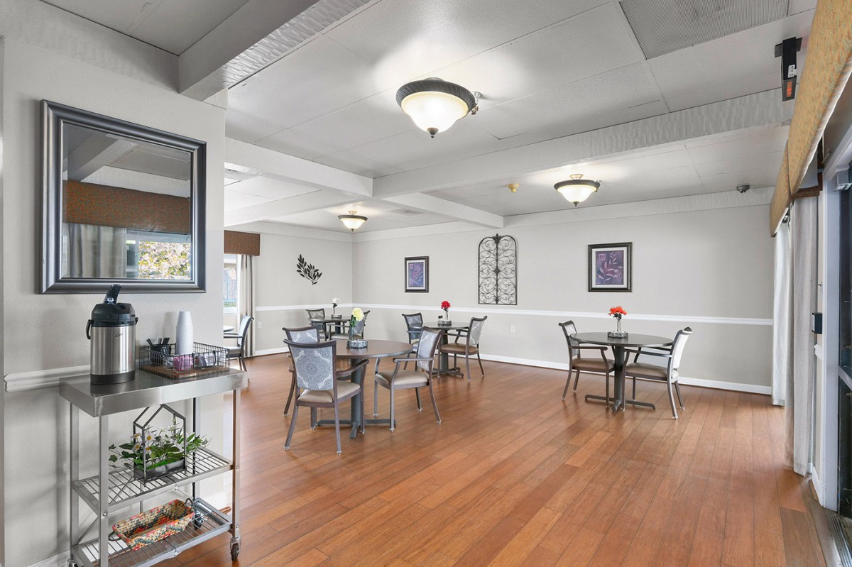 A bright dining area with tables and chairs on a hardwood floor, featuring modern lighting and simple decor.