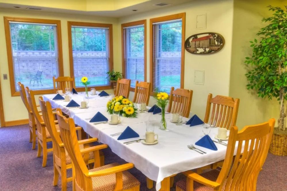 A well-set dining table with wooden chairs and floral decorations by the windows.